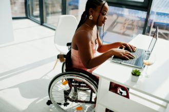 Young disabled African American woman in wheelchair at home working with laptop.